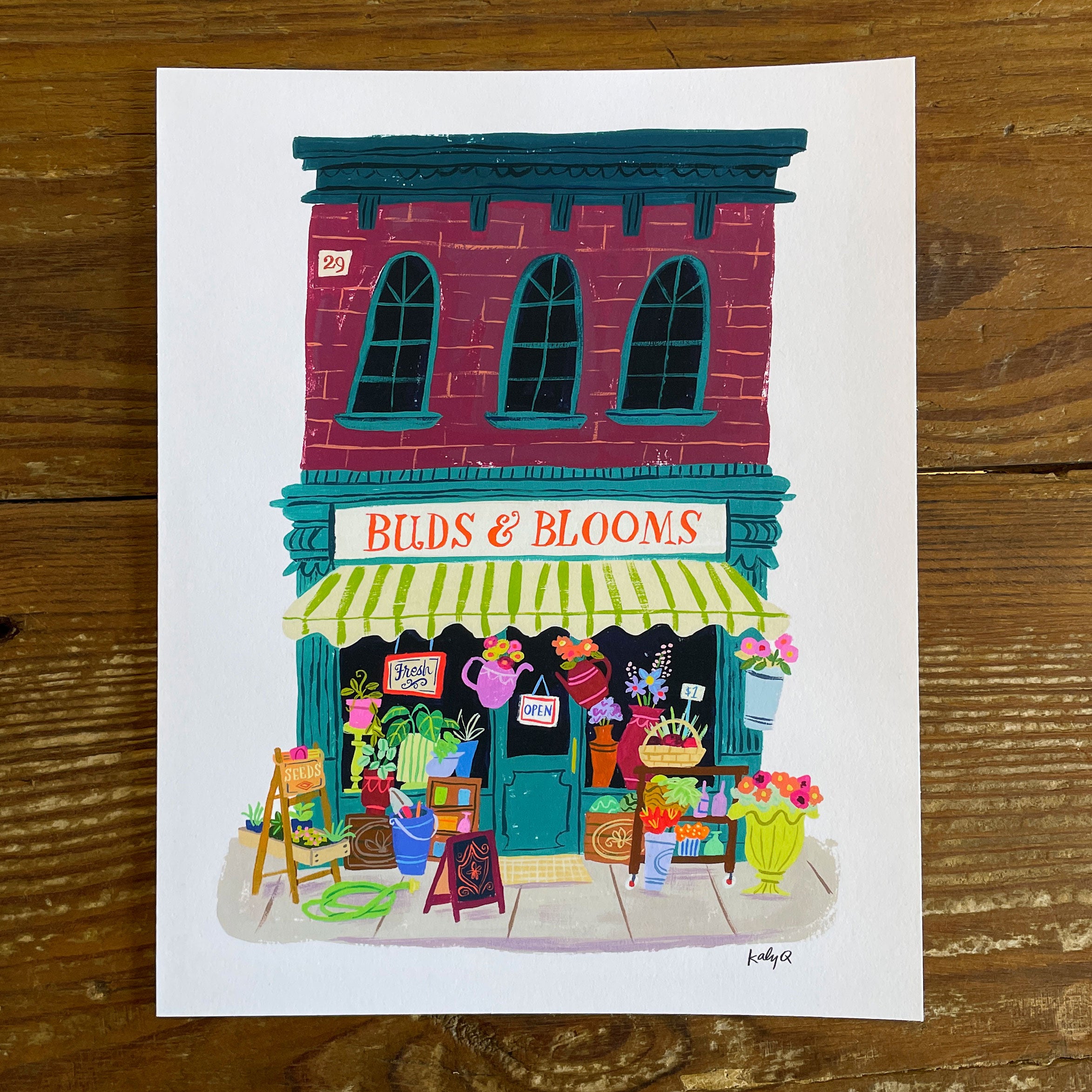 Illustration of a vintage flower shop storefront with colorful window displays & flowers, hand lettering reads Buds and Blooms