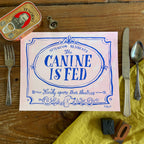 Illustration of a decorative Victorian-style sign on a pale pink background, blue hand lettering reads Attention Residents: The Canine is Fed, Kindly Ignore Their Theatrics